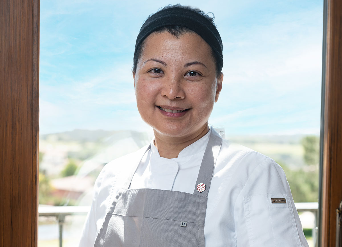 Sarah Ramos wears a white chefs smock and a gray apron.