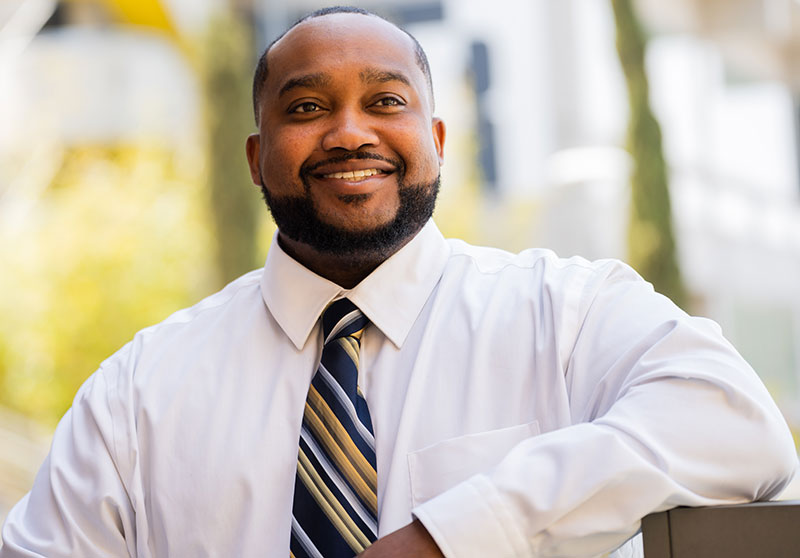 George Buchanan wears a white button down shirt and a blue and gold striped tie