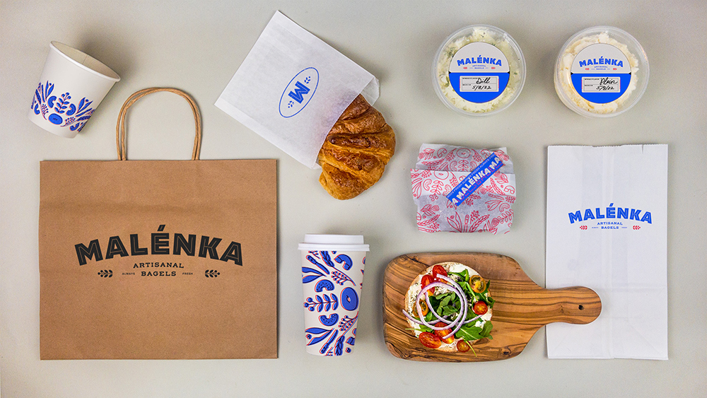 Malenka food brand shows a brown paper back with the Malenka logo with Greek food displayed with Malenka brand packaging.