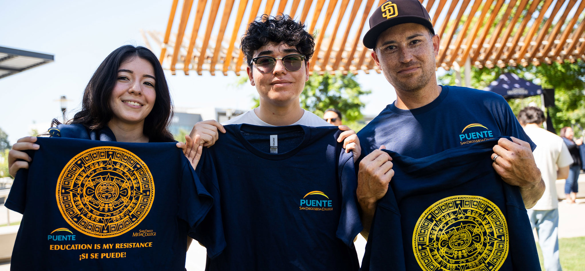 Students in the Puente Project hold up navy blue T shirts that say Puente and have an Atec seal on them.