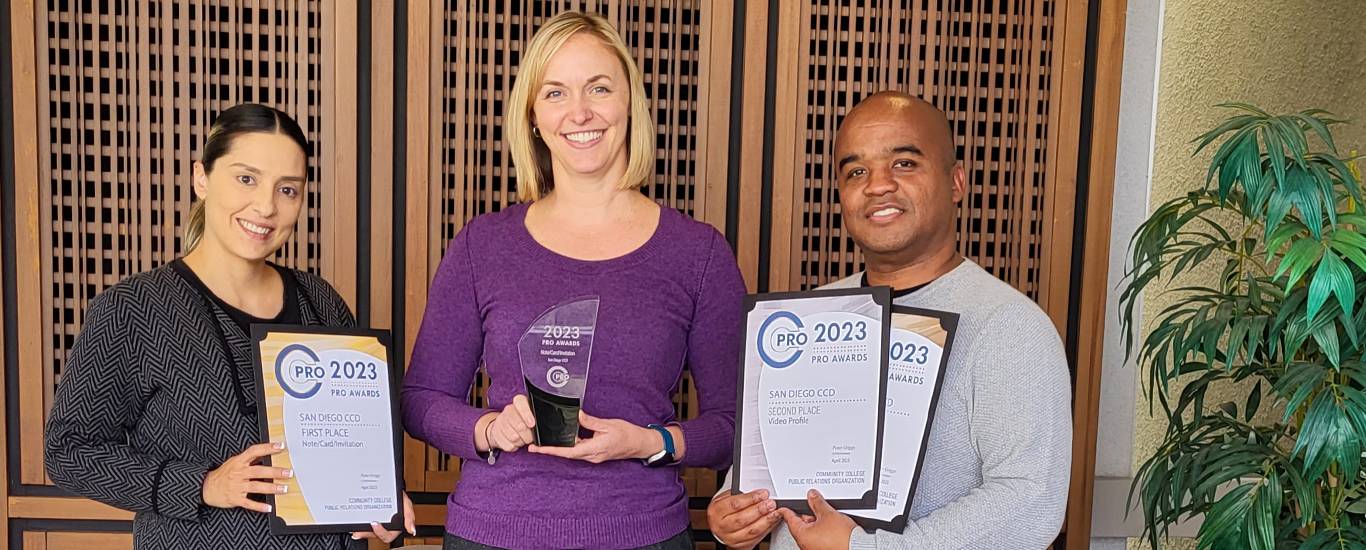 Three employees hold up the four awards. One is a glass award and the other three are on parchment paper