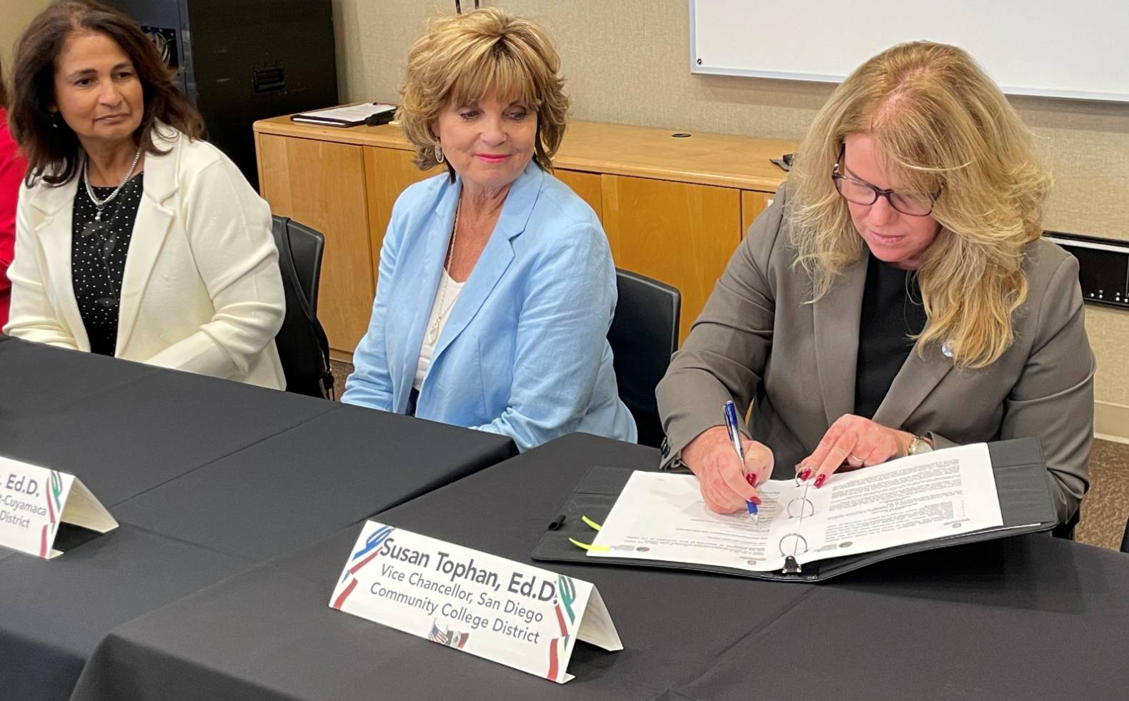 Susan Topham signs a document while two women look on