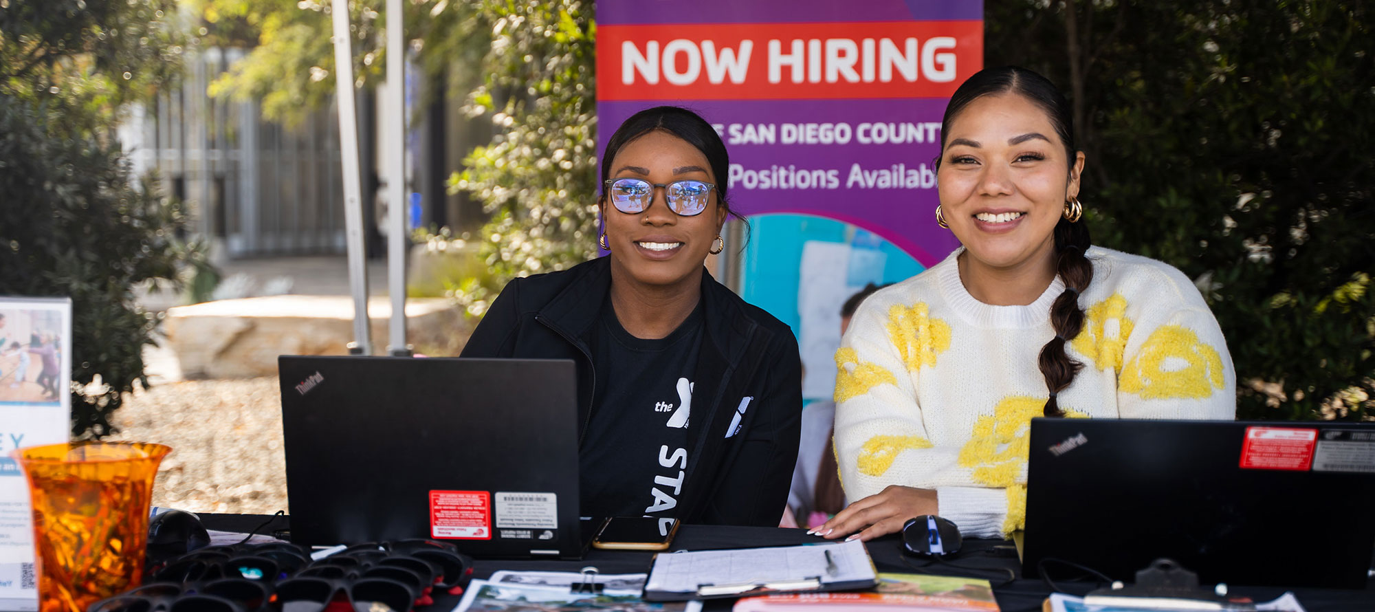 Two women sit at the booth for the YMCA at a previous job fair