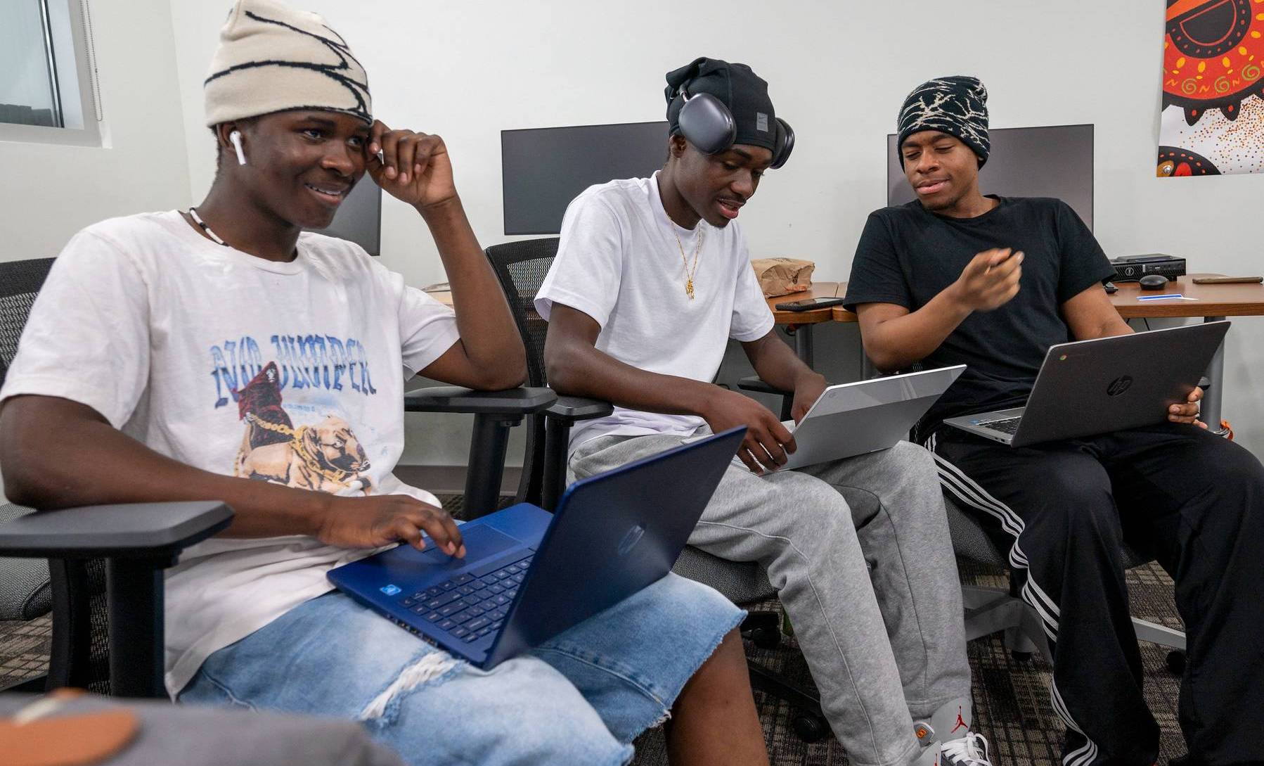 Three students sitting in a classroom with laptops