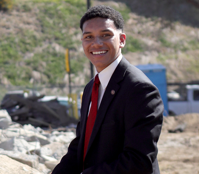 Diego Bethea is outside wearing a black suit and a red tie