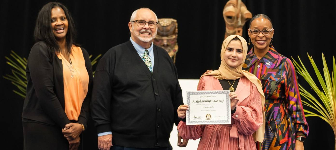 Husna Ayoubi on stage with three other people holds up the scholarship paper