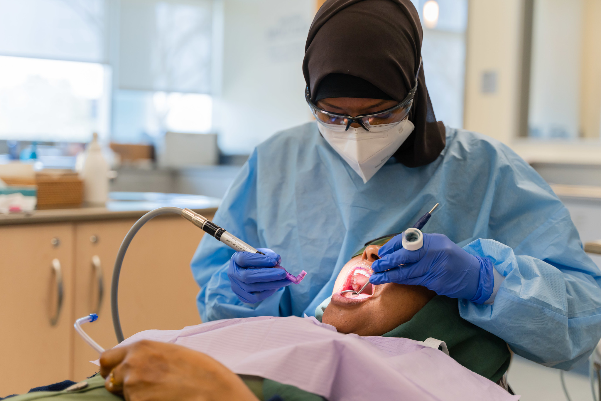 A dentist in blue scrubs is working on a patient in a dental chair