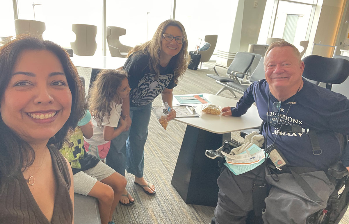 Four people at the new terminal one at the airport. One of them uses a wheelchair. 