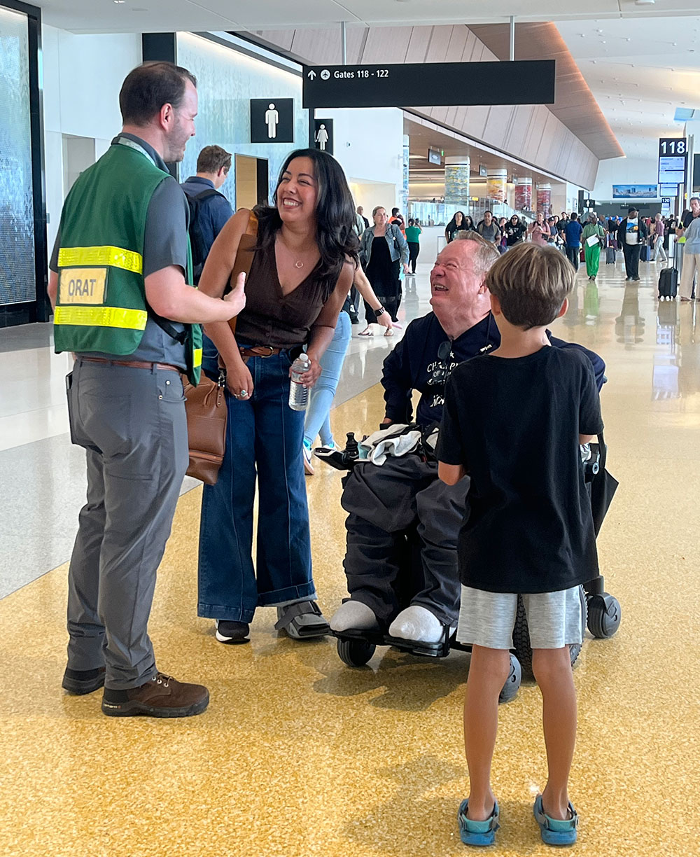 Four people at terminal one stop to talk to an employee. One person is using a wheelchair.
