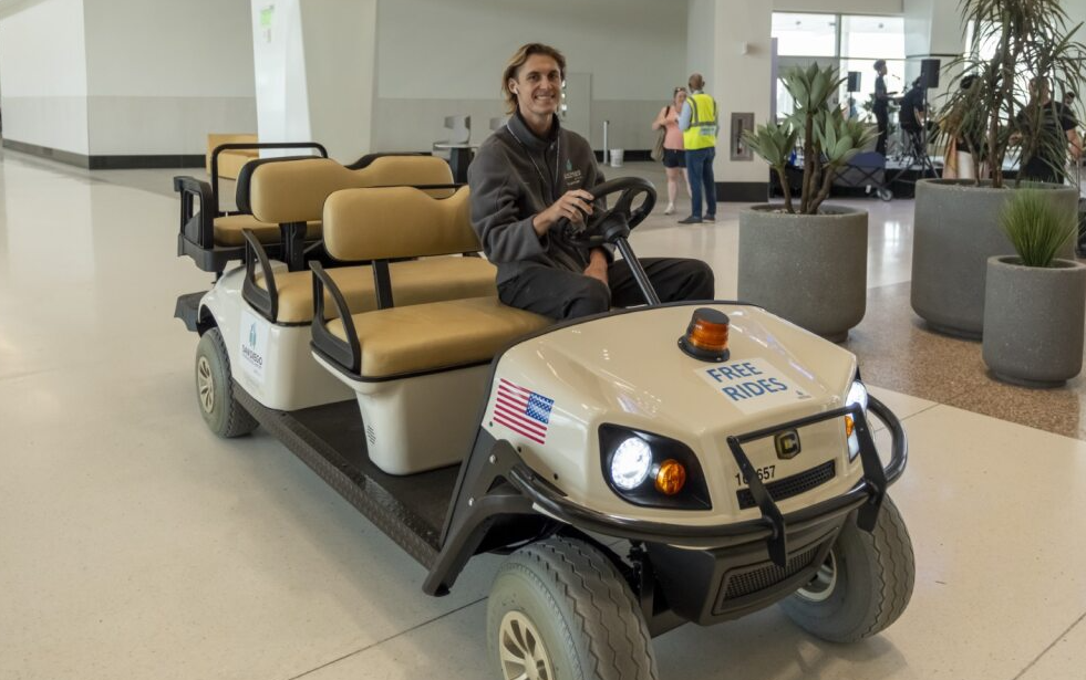 A man driving a cart in the terminal to give free rides to passengers who need assistance getting to their gate.