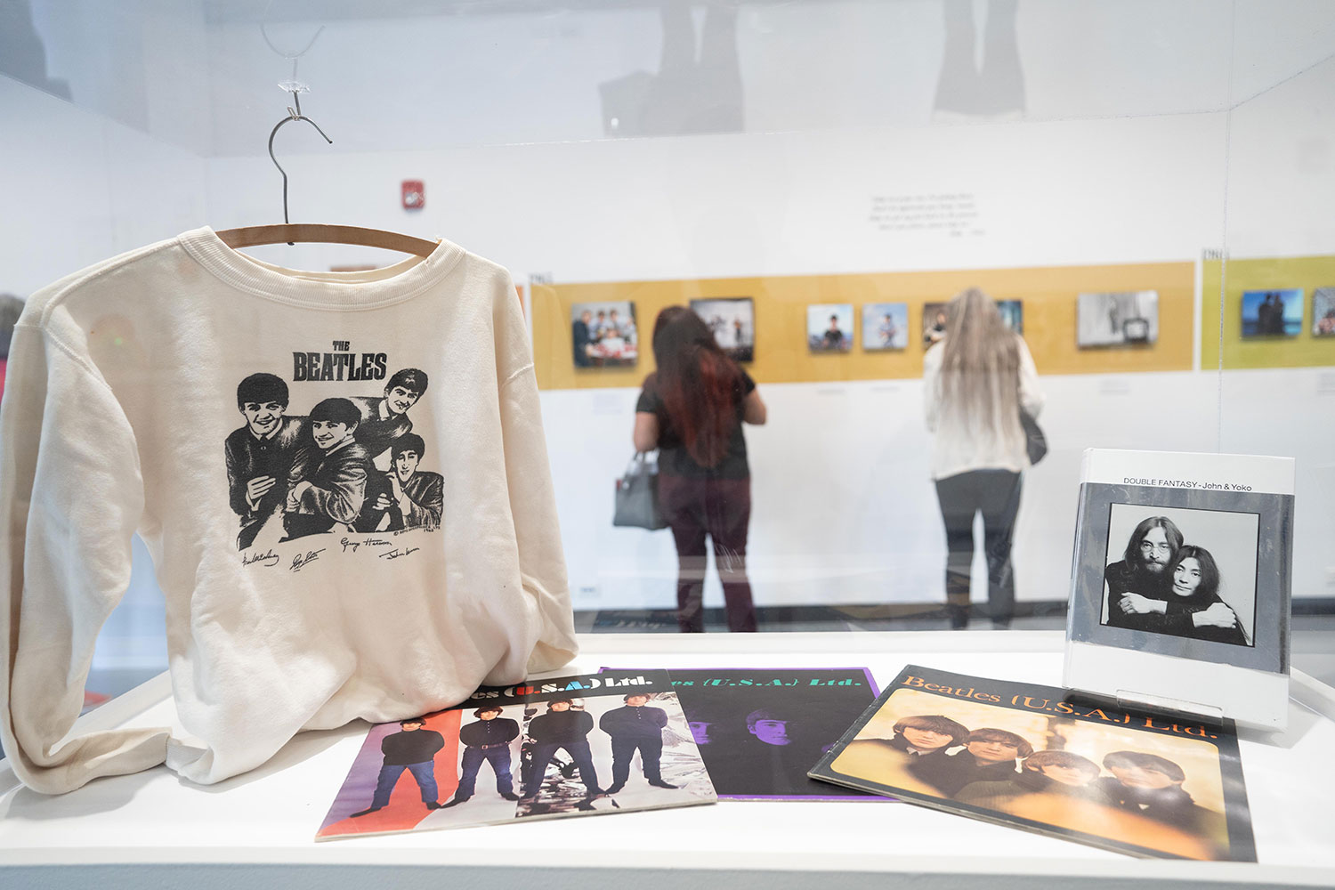 A white sweatshirt that says Beatles and a picture of the band. Color photographs of the band and a photo of John and Yoko in a display case