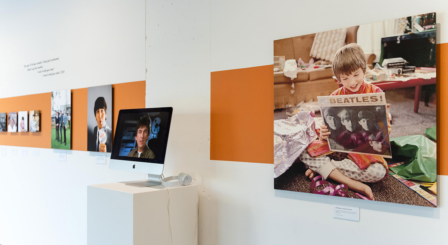 A row of Beatles photos on a wall with orange accents around the photos. One photo is a boy smiling and holding a Beatles album