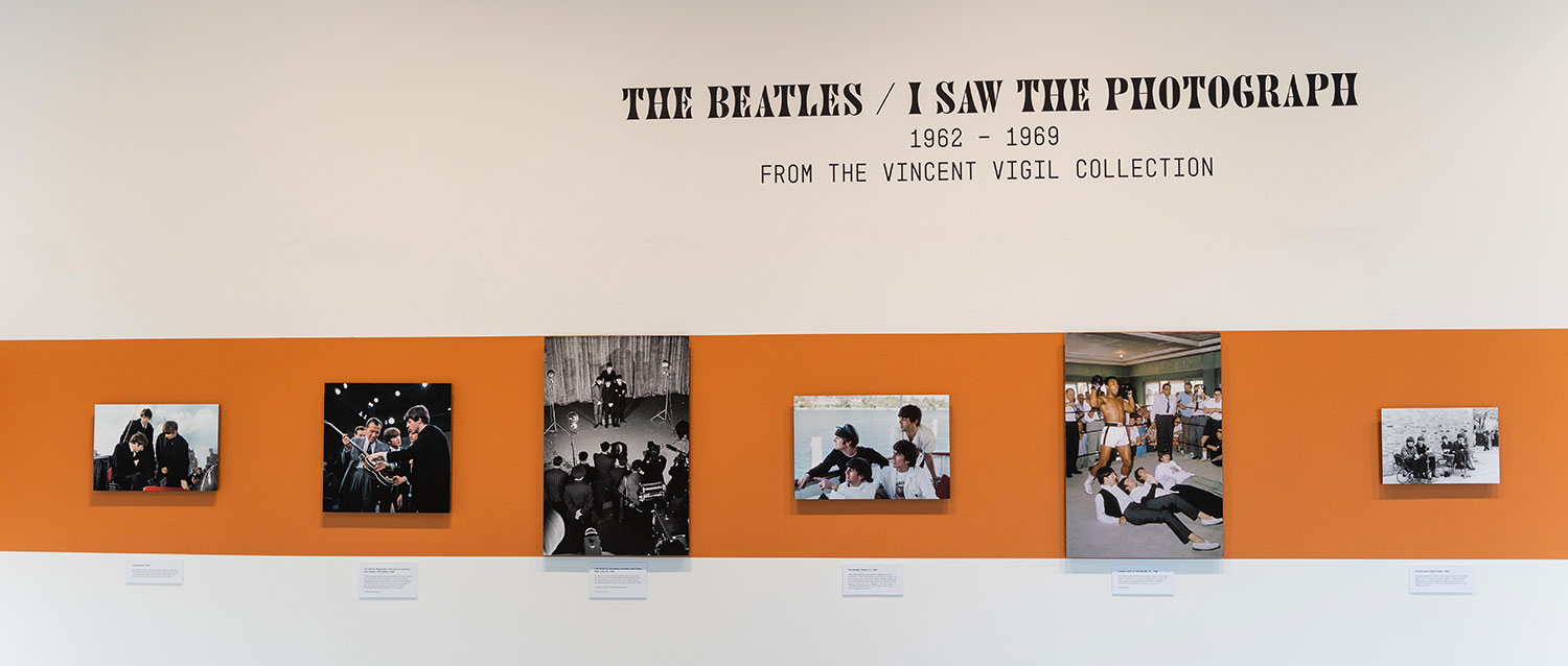 A strip of orange across a wall with four Beatles photos text on the wall above says The Beatles I saw the photograph