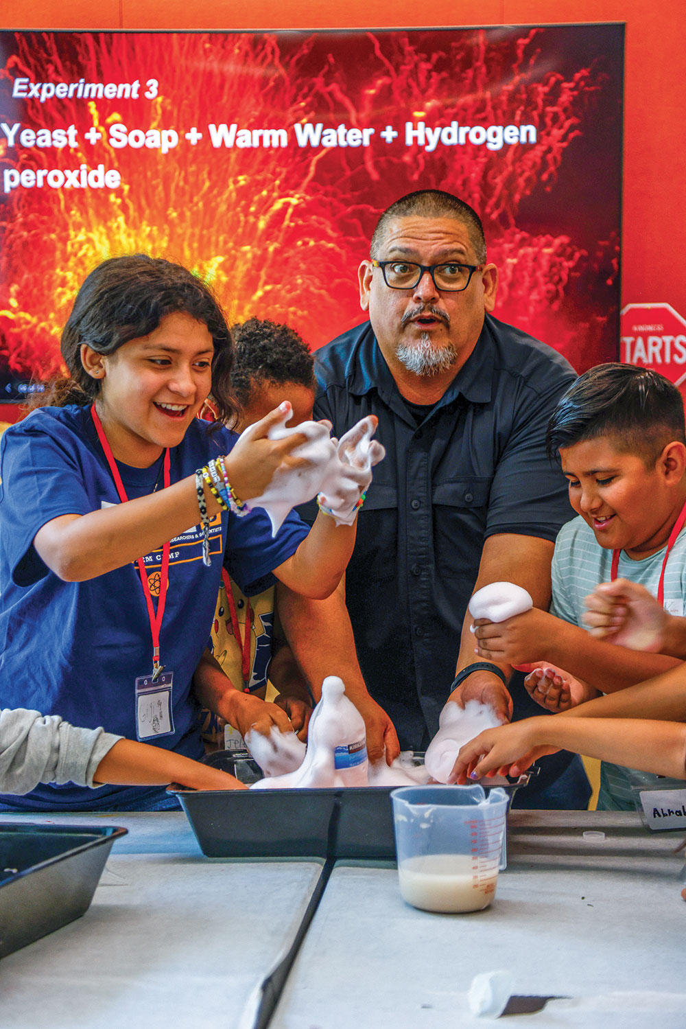 Beto and 3 kids put their hands in a bucket of foam during a science class