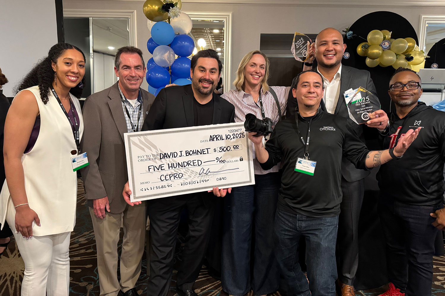 Seven people at the award event including a student holding up a giant scholarship check for $500