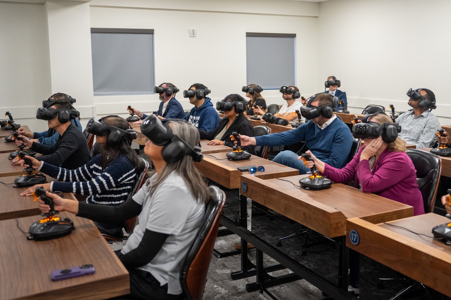 A classroom of people wearing virtual reality goggles and using joysticks
