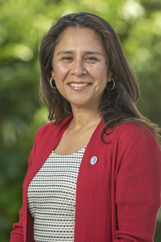 Portrait photo of Geysil Arroyo wearing a red sweater with greenery in the background.