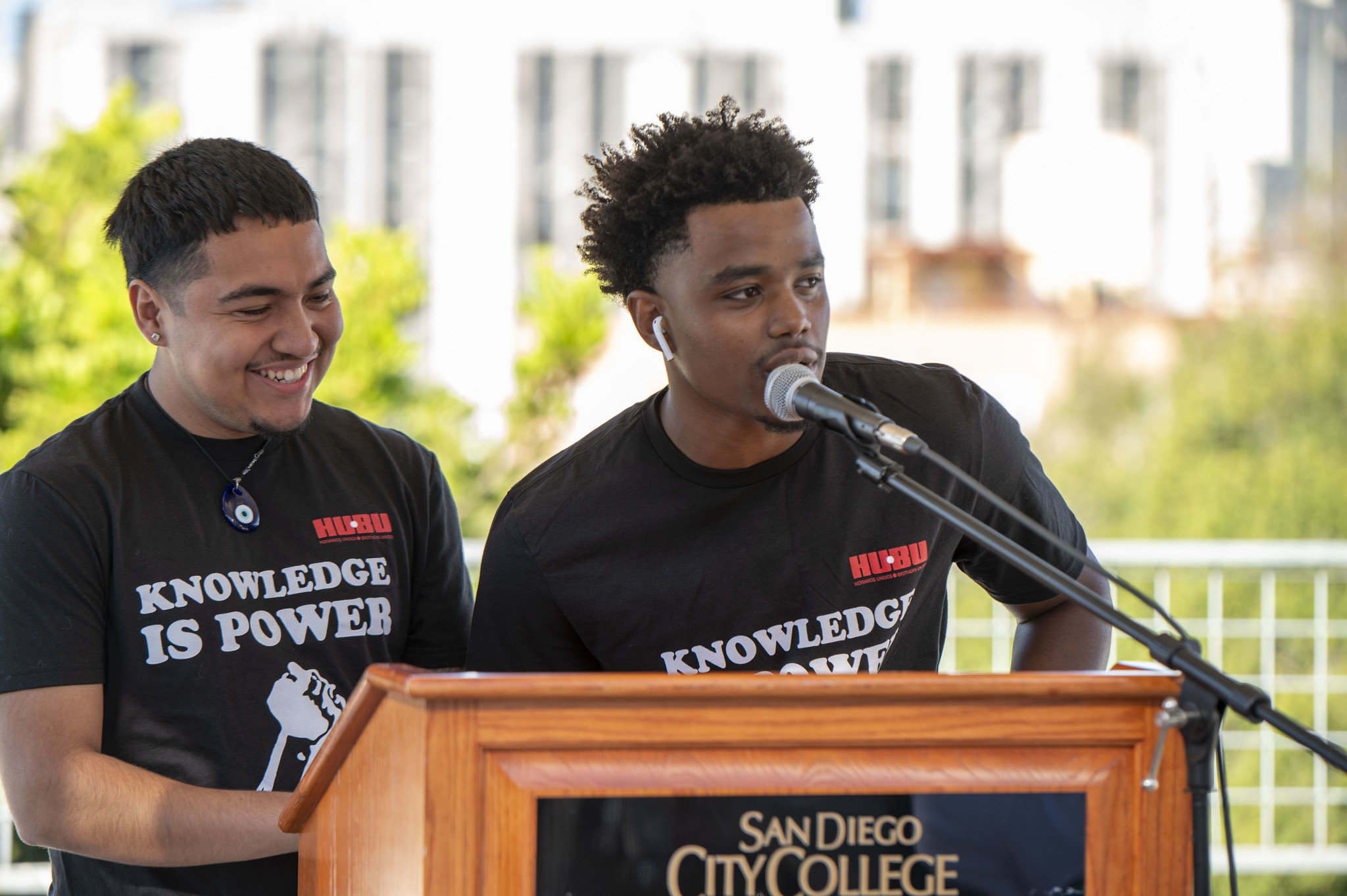 Two students standing a podium wearing black tee shirts that say knowledge is power with a red HUBU logo.