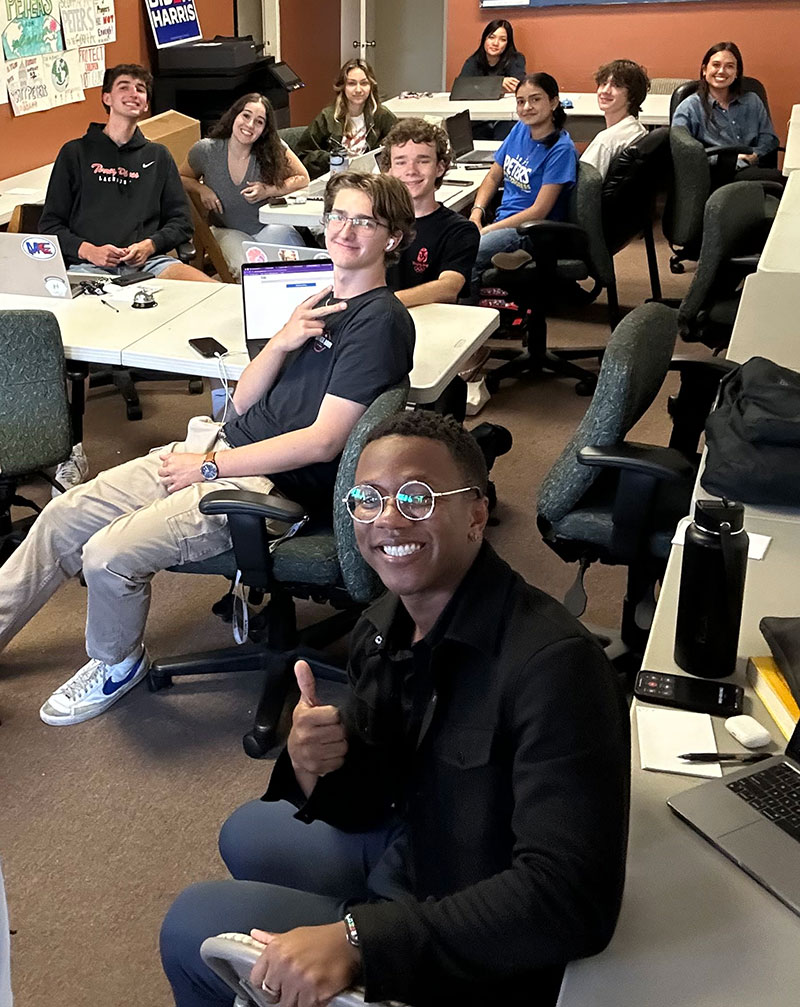 Ten interns sitting around a table. Angel Wilson is in front giving a thumbs up