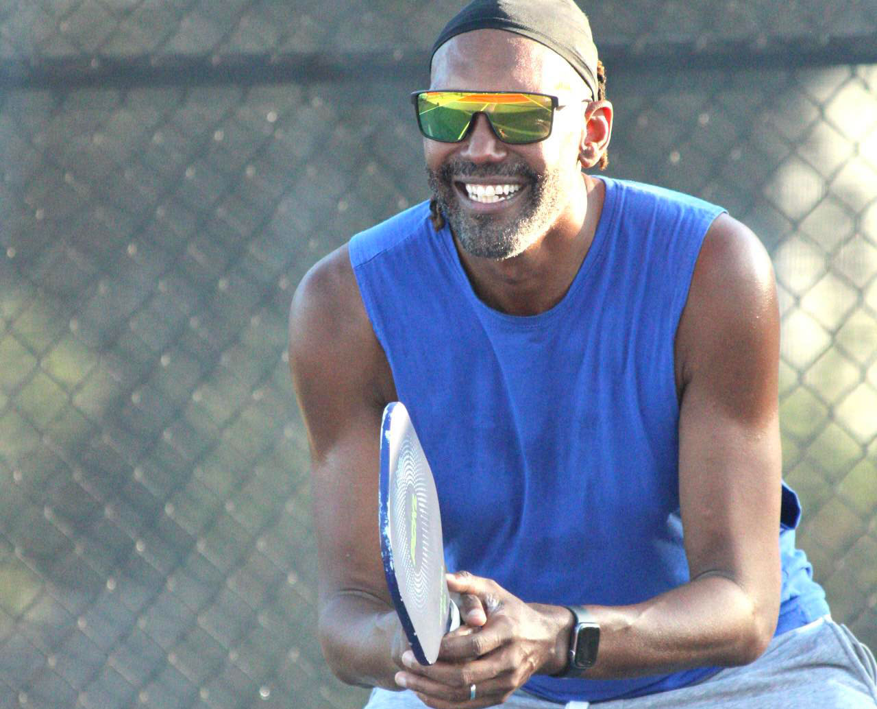 Jesse Jones in a blue tank top holds a racket on a pickleball court