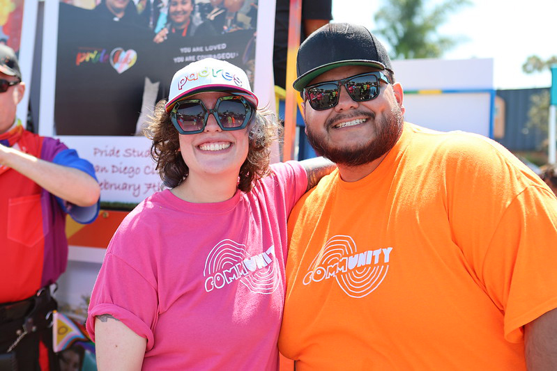 Two employees wearing orange and pink t shirts at the 2024 Pride Parade