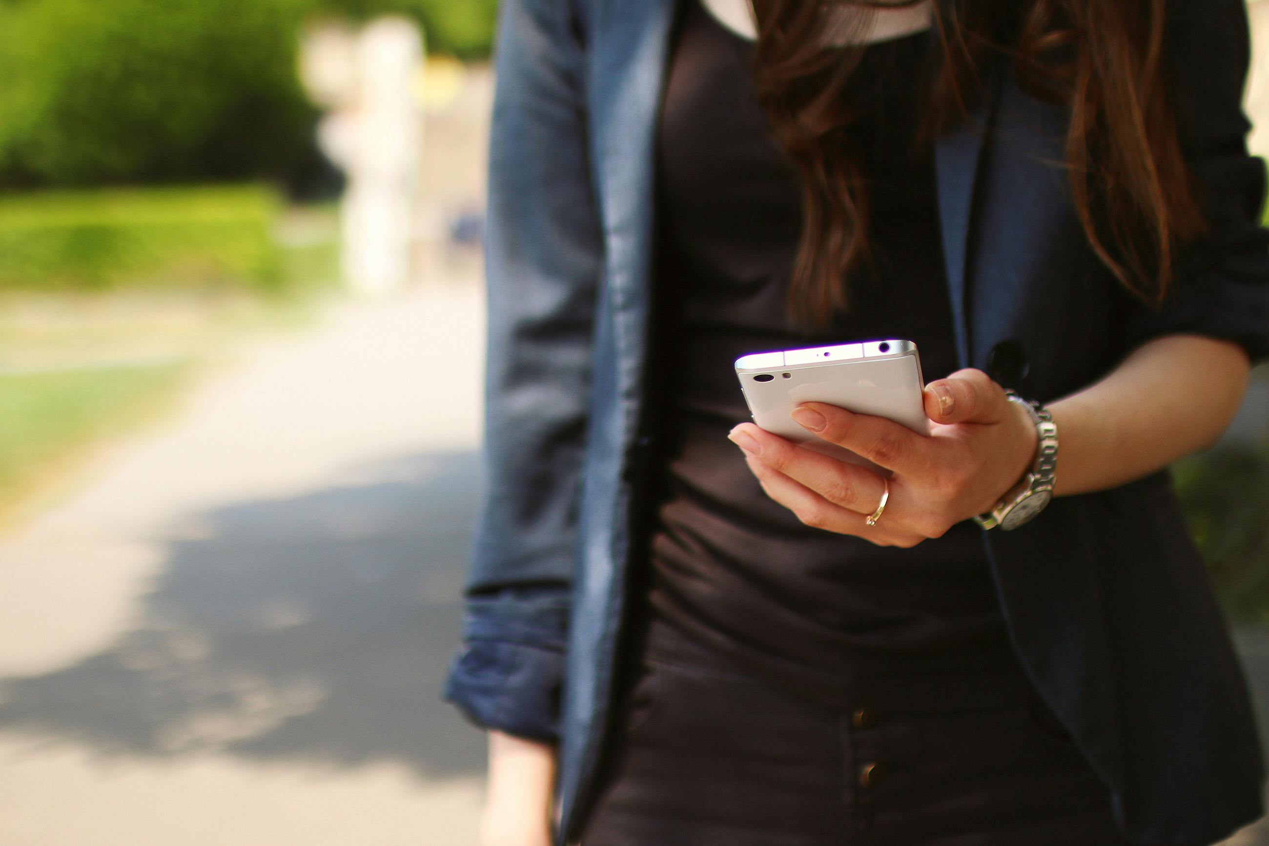 A closeup of someone walking and looking at their cell phone.