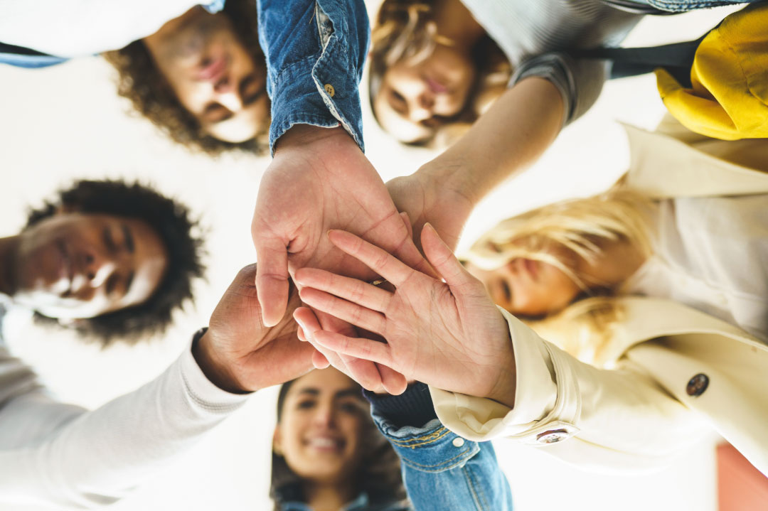 Six people stand in a circle and put their hands in the middle on top of each others