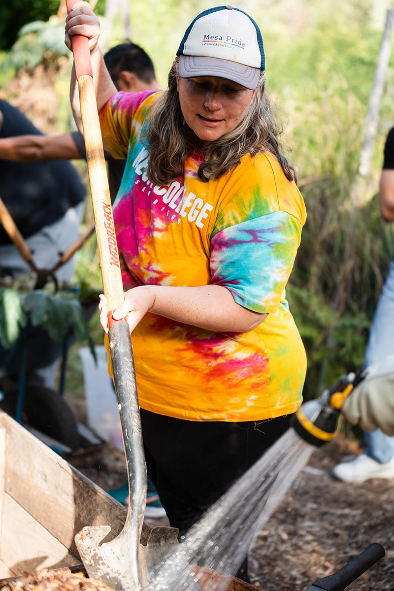 Waverly Ray in a rainbow tie dye shirt digging with a shovel in a garden