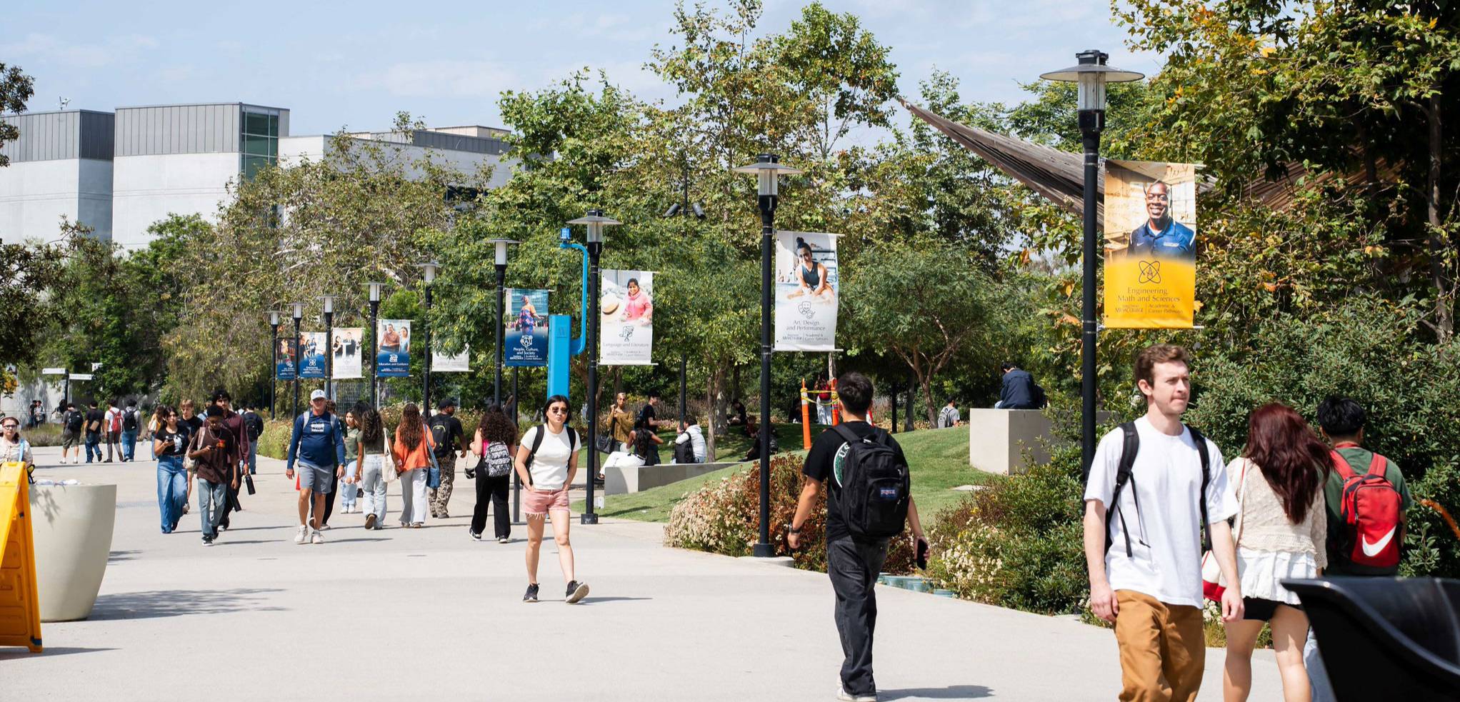 Dozens of students walking on Mesa Campus with buildings and greenery in the background.