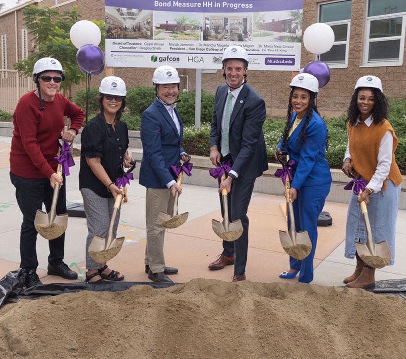 Six people with shovels scoop dirt at the groundbreaking.