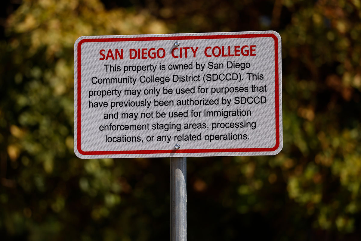 A white and red sign along a pathway at City College