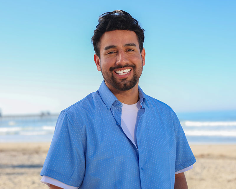 David Pradel wearing a blue button down shirt with the beach in the background.