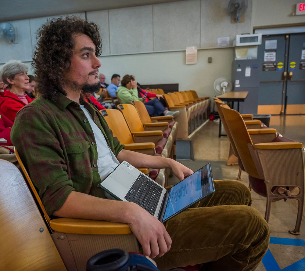 City College alum Jakob McWhinney sitting in a classroom with a laptop on his lap