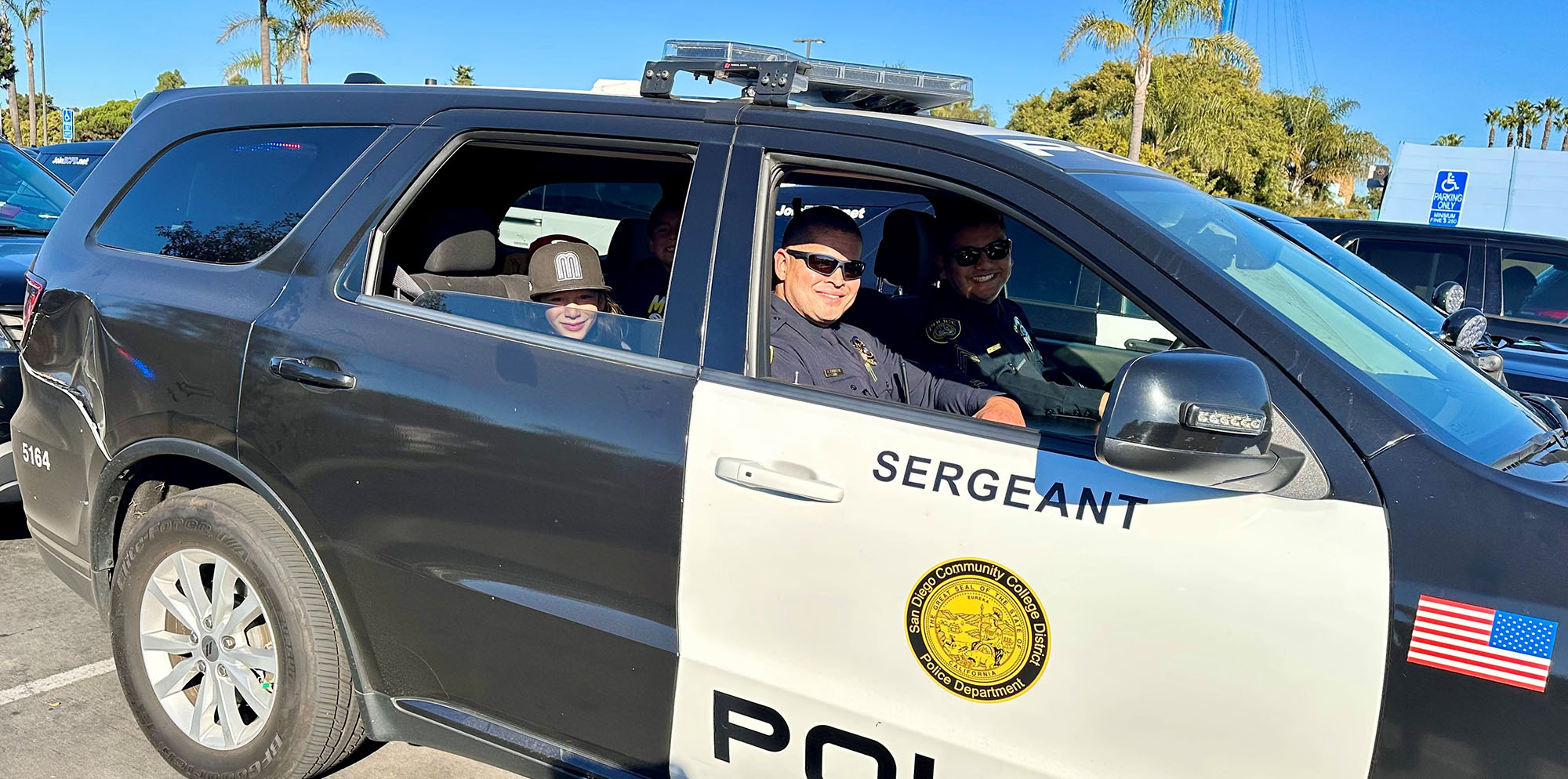 A child in the back seat of a police SUV. Two officers are in the front.