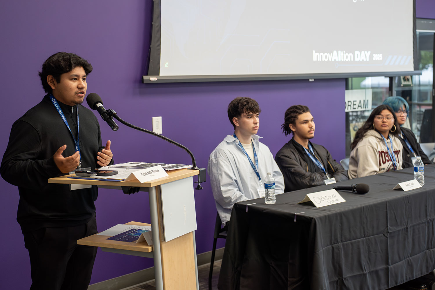 
A student at a podium speaks with a panel of four next to him.
