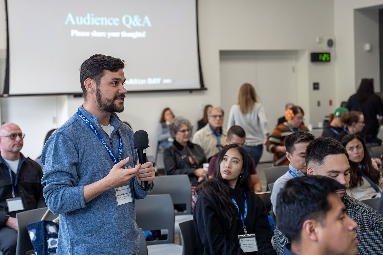 
A member of the audience stands and speak into a microphone.

