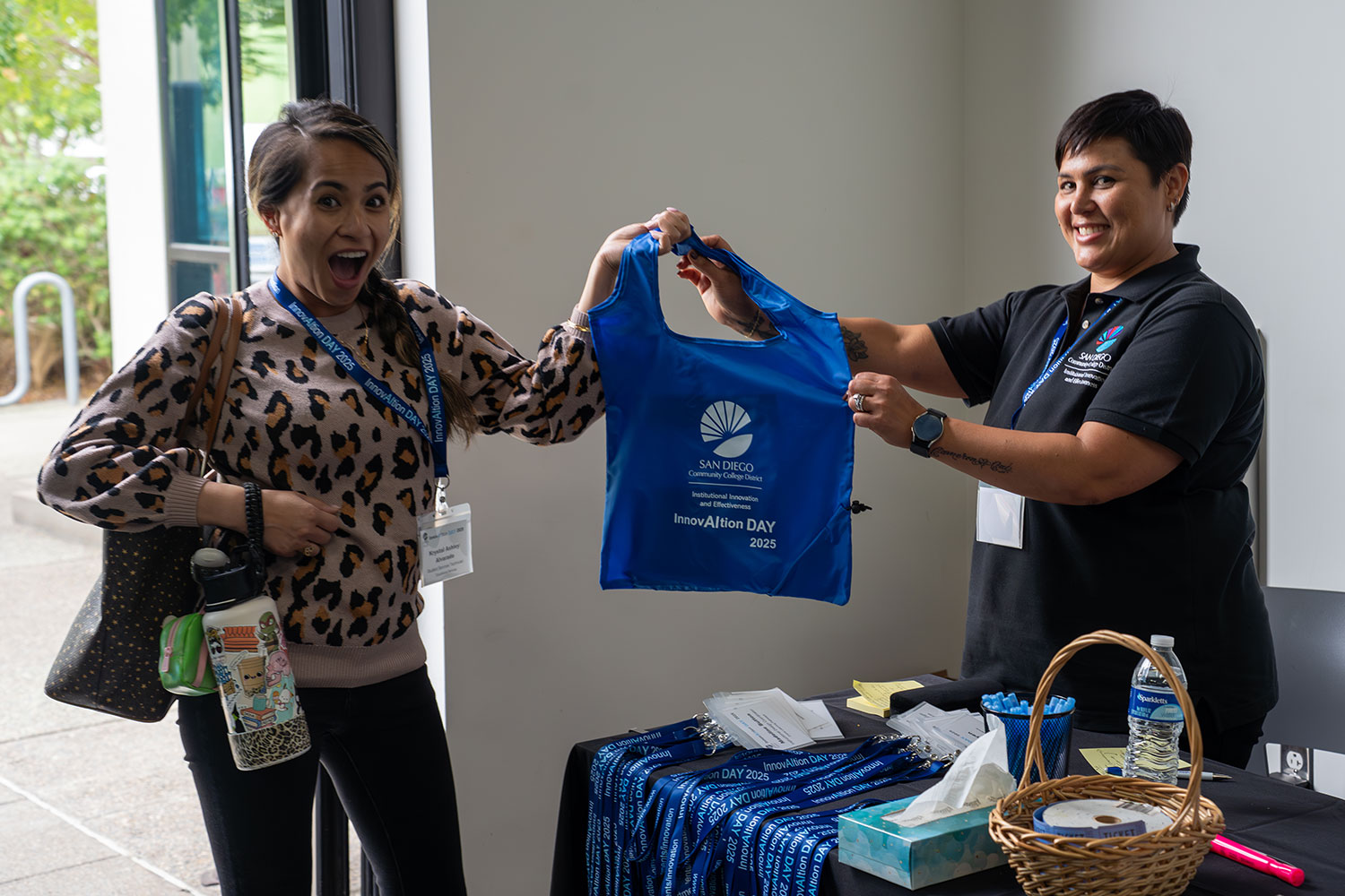 
Two people hold up a blue canvas bag with the district logo that was distributed at the event
