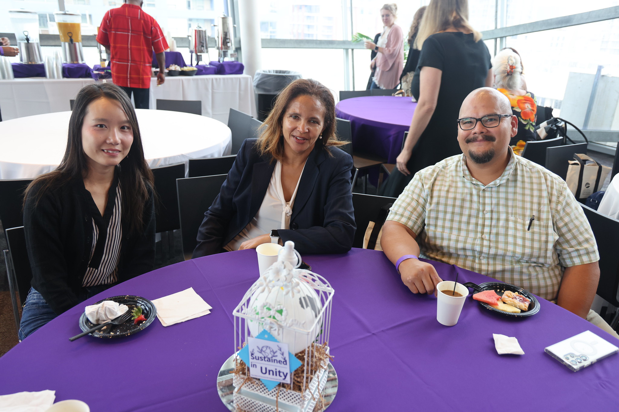 
Three people sit at a table with a purple table cloth at the lunch following convocation.

