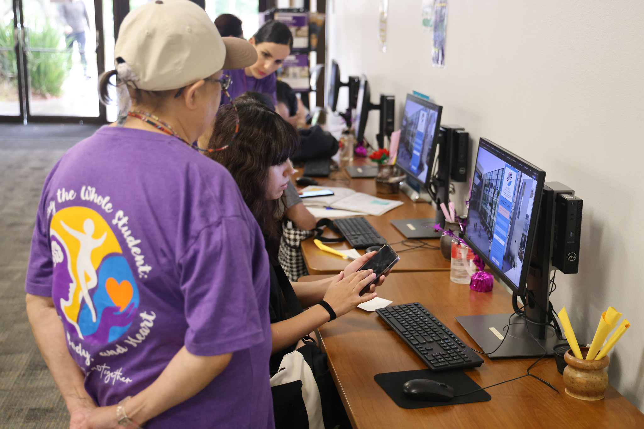 
Employees standby to assist as a row of students sit at a table and work on computers.
