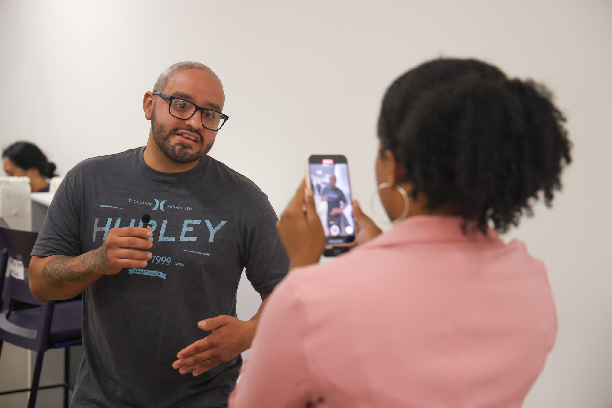 
A woman using her phone to record a man speaking.
