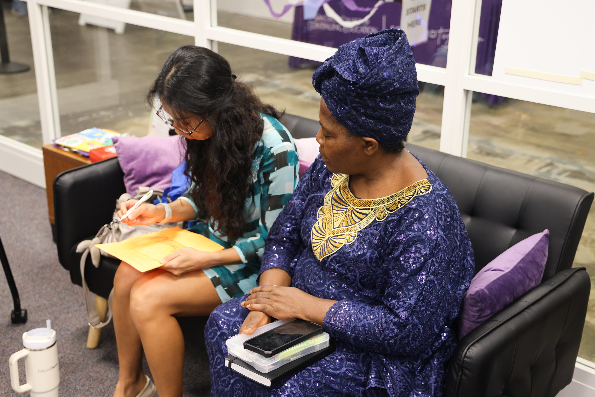 
Two women sitting on a couch. One is filling out a form. 
