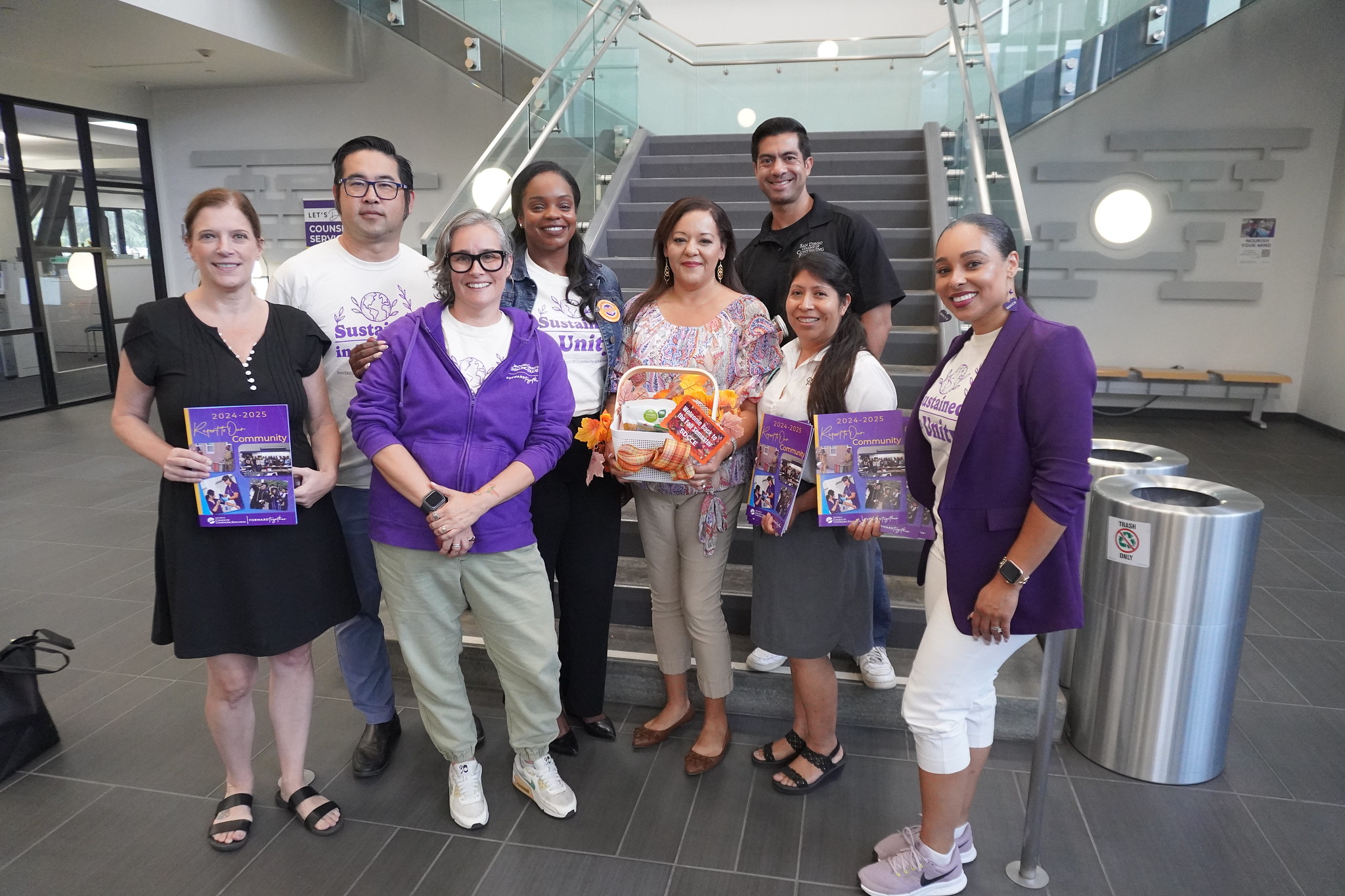 
President Tina King with seven employees in front of a staircase on campus. 
