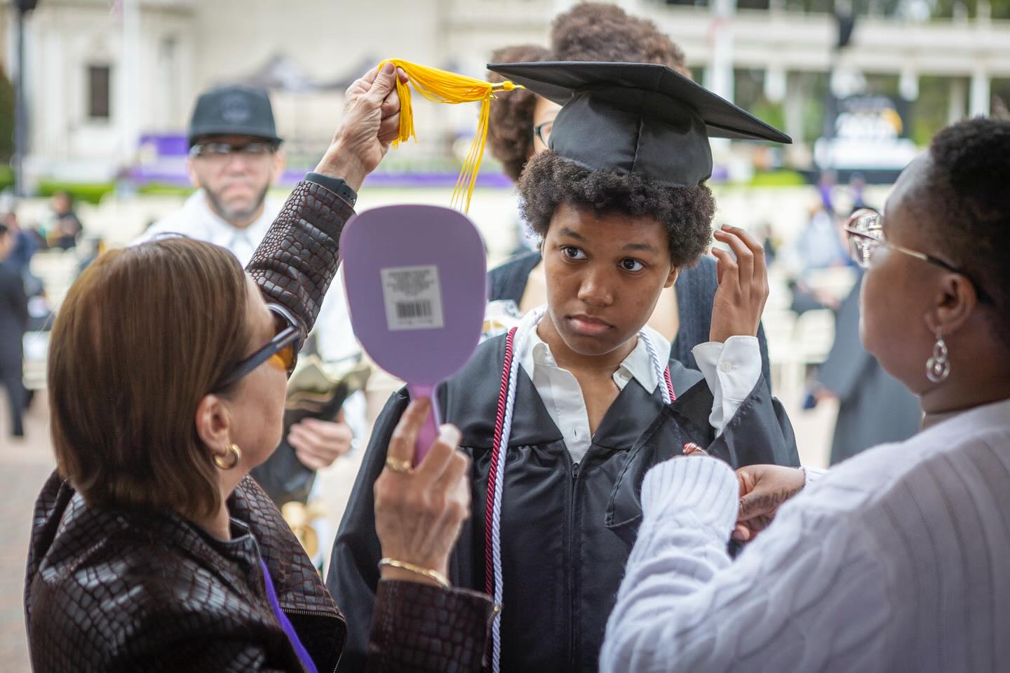 
A graduate getting ready looks at himself with a mirror as he puts his cap on.
