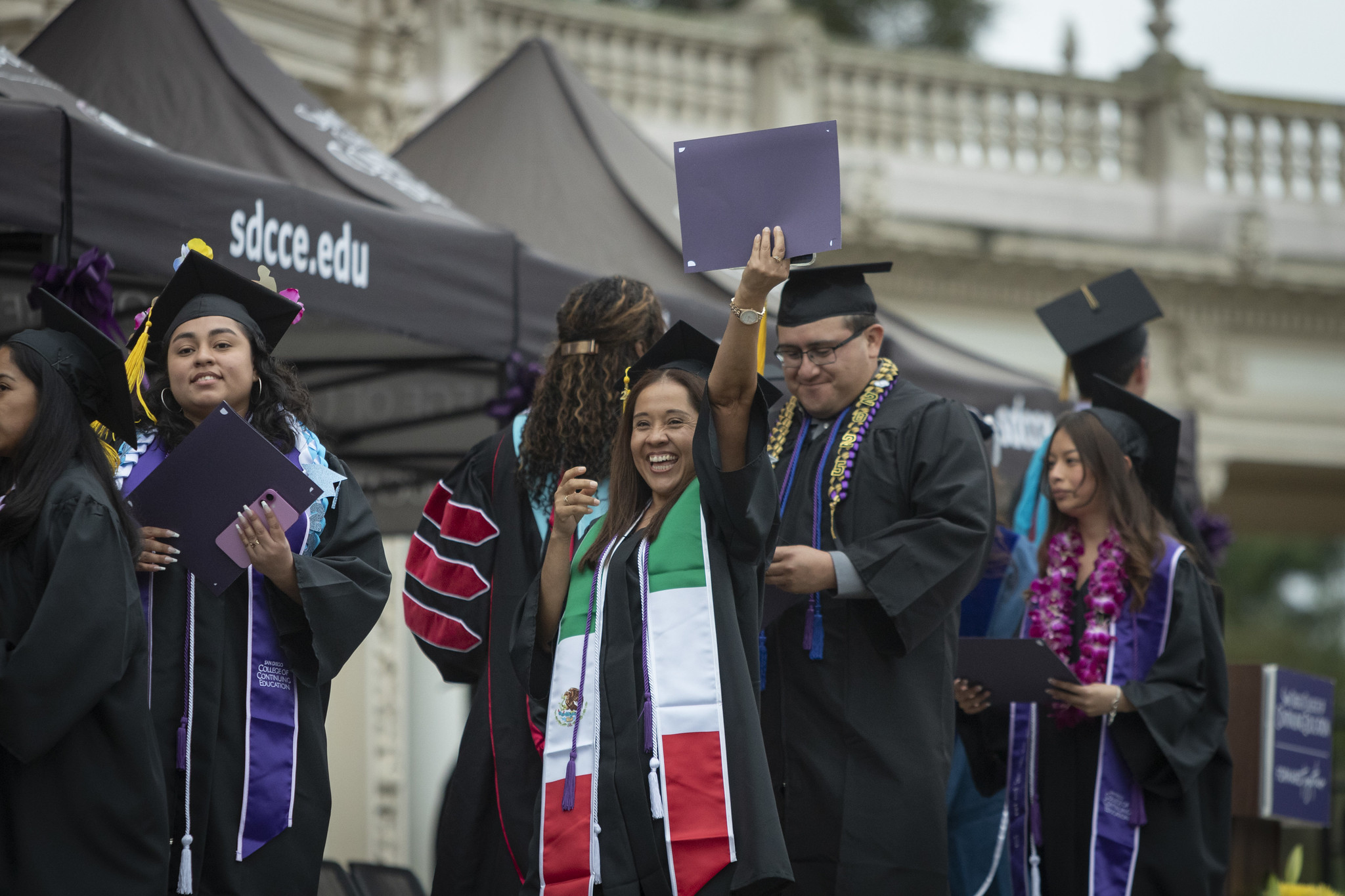 
A graduate on stage smiling holds her certificate over her head.
