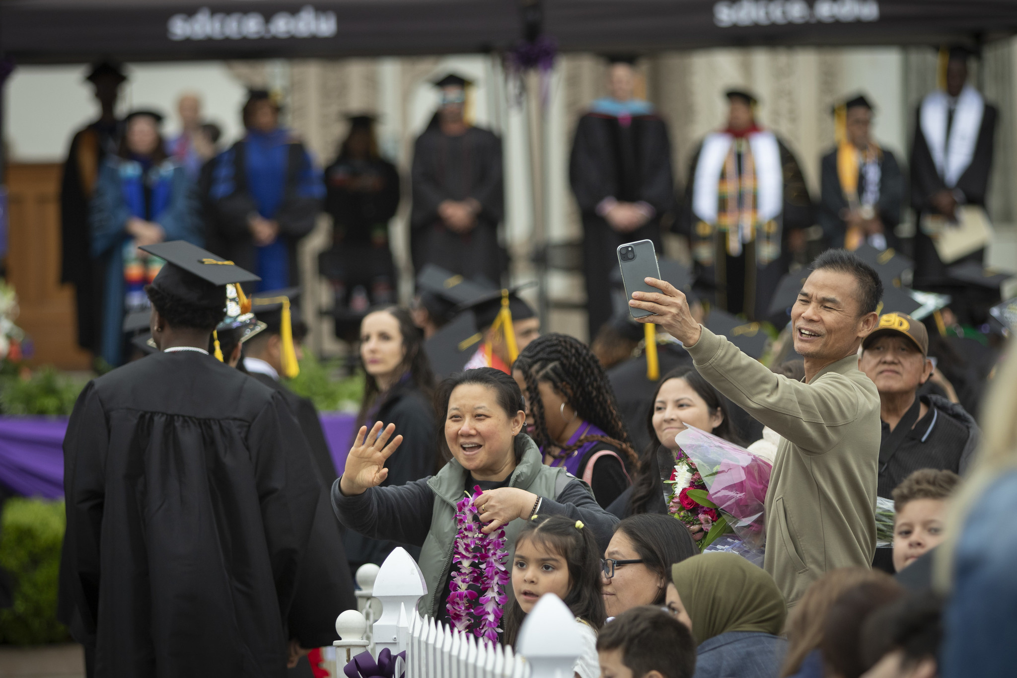 
Family and friends in the crowd waving and taking pictures with their cell phones.
