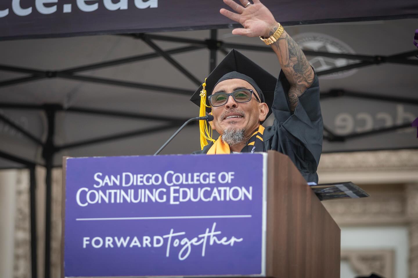 
A student commencement speaker at a podium waving to the crowd.
