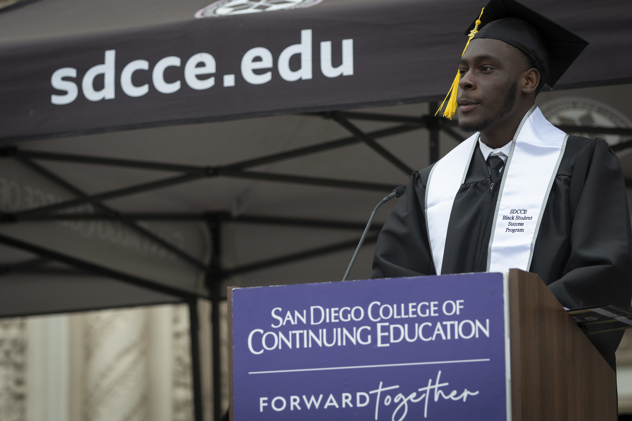 
A student speaker on stage at a podium addressing the crowd.
