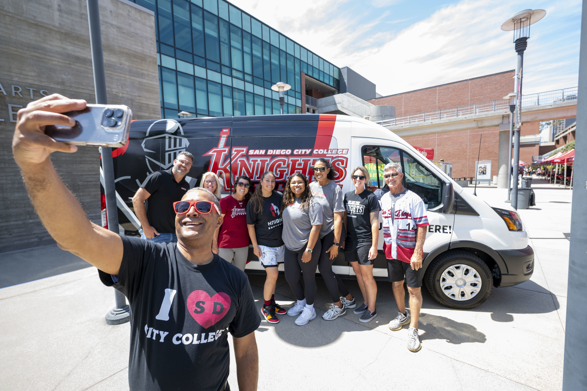 
City College President Ricky Shabazz takes a selfie with eight employees next to a City College Knights van.
