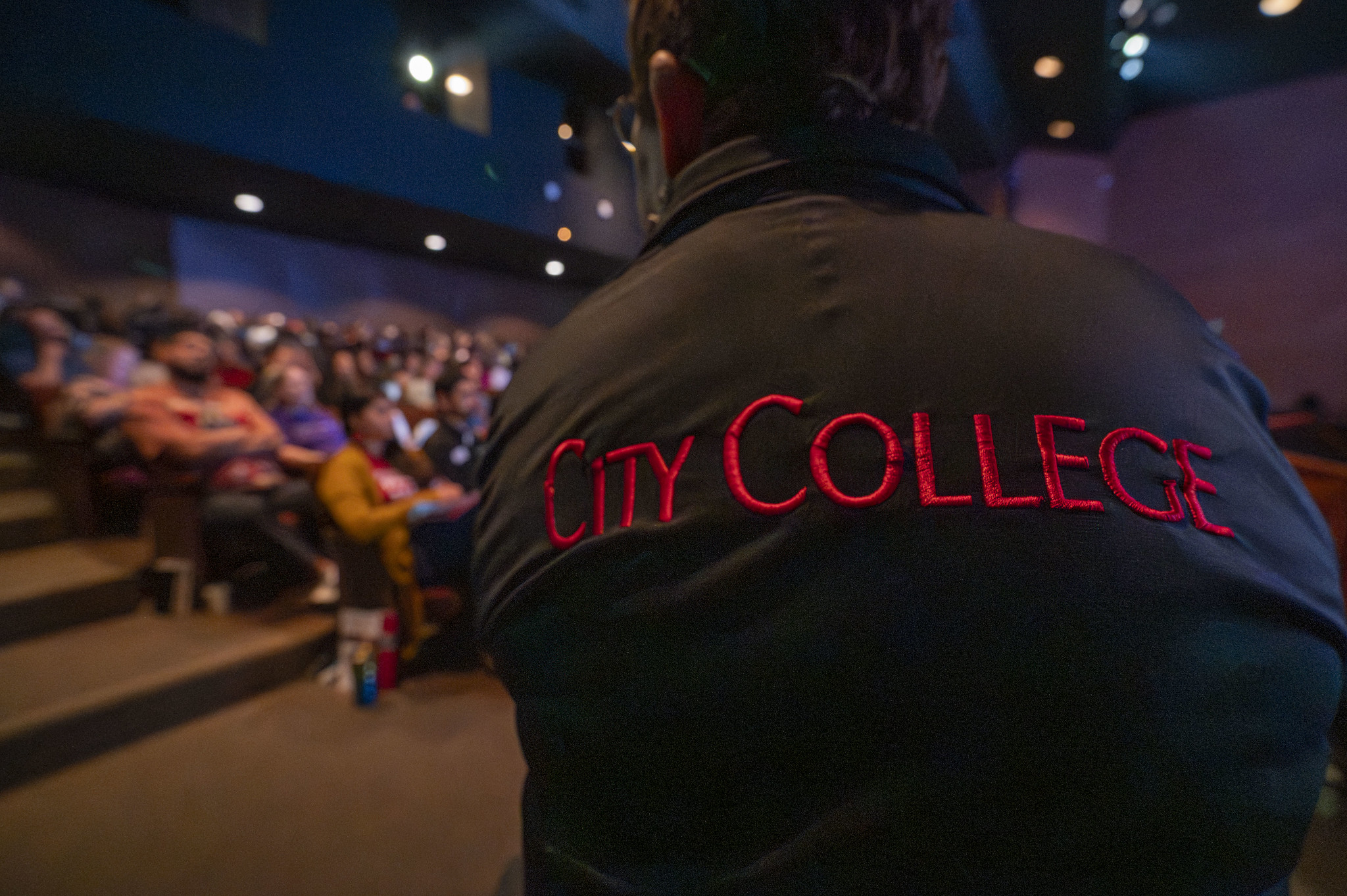 
A person listening to the presentation is wearing a black jacket with City College in red across the back.
