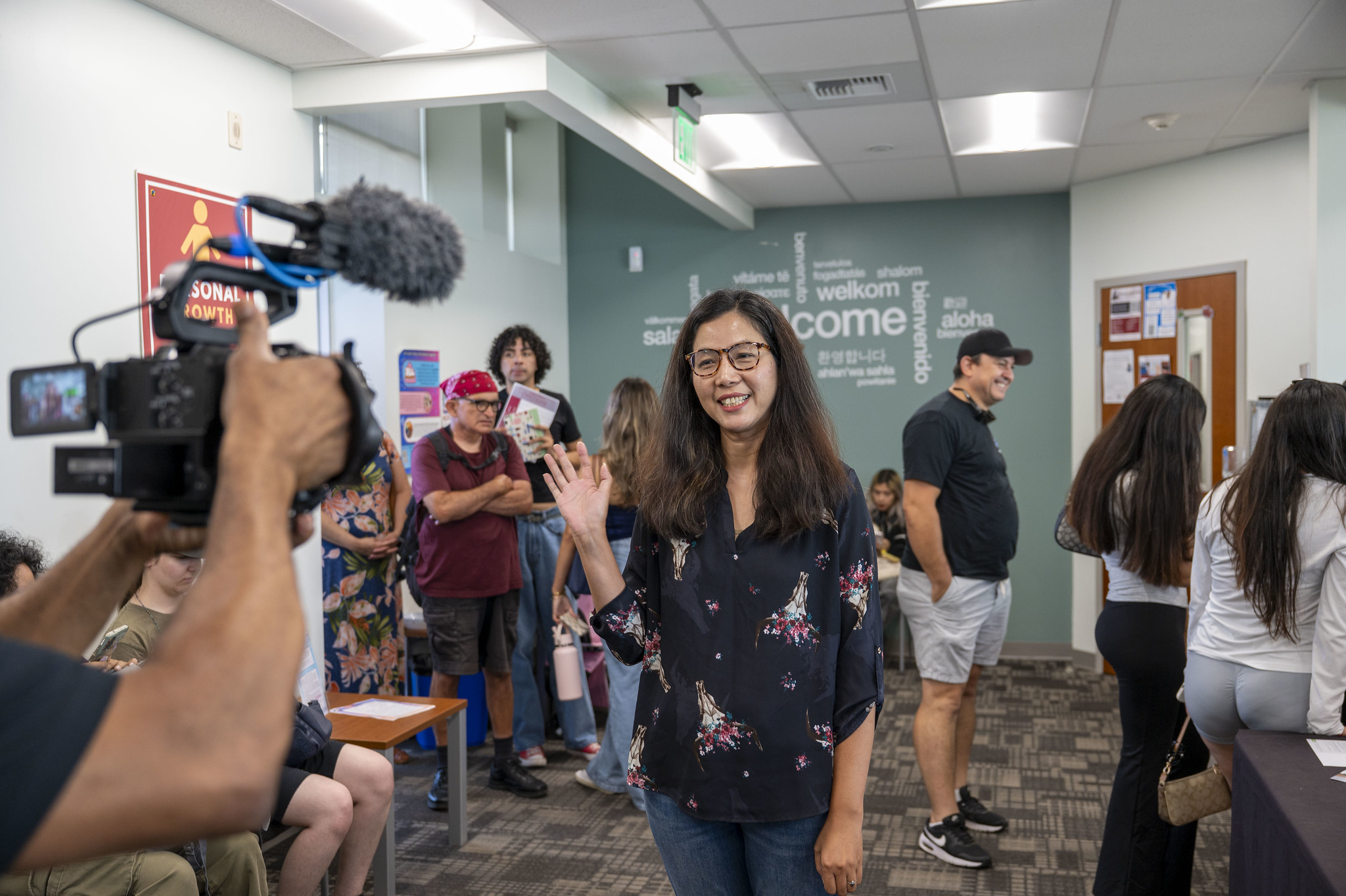 
A woman is being recorded on video. There are students standing in line background.
